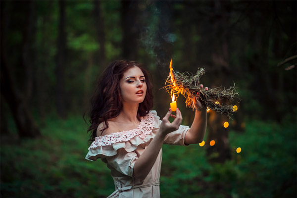 Frau die im Rahmen eines Rituals im Wald getrocknete Pflanzen anzündet